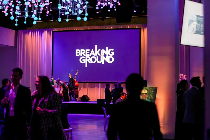A cellist plays in front of a screen showing the Breaking Ground logo during their annual gala.